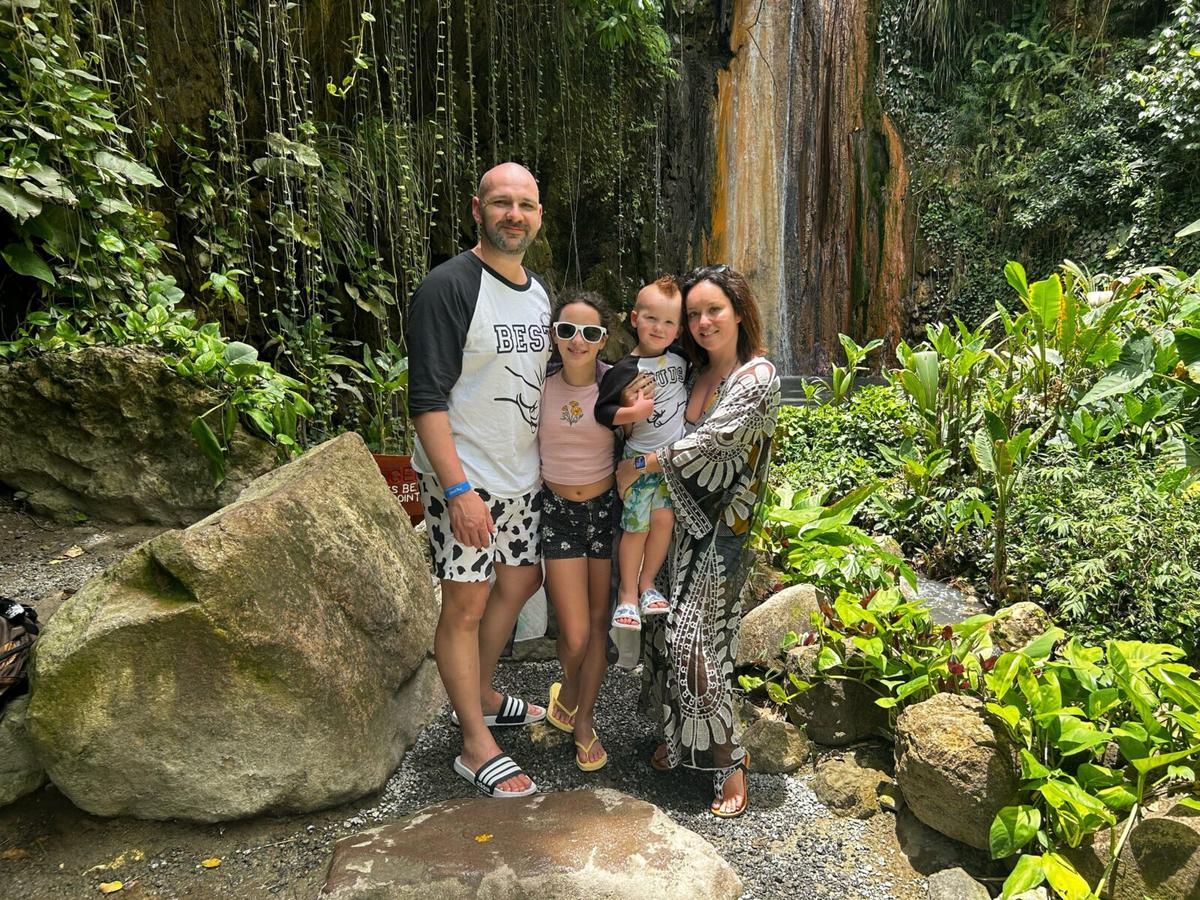 A Caucasian family is standing near a waterfall in a forest.