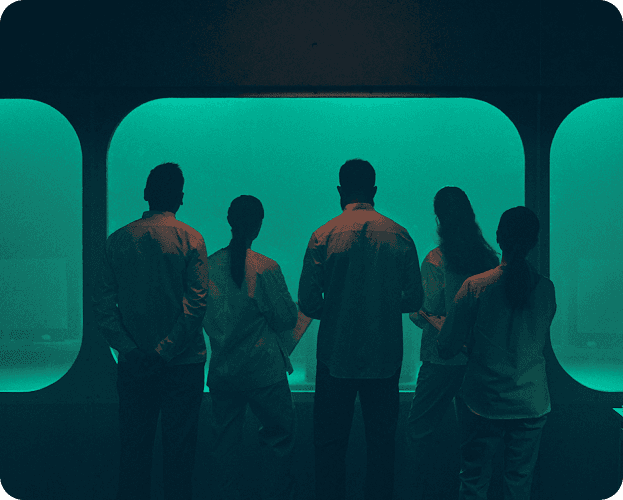 Group of people in a warm, heated room looking out a window at dreary weather.