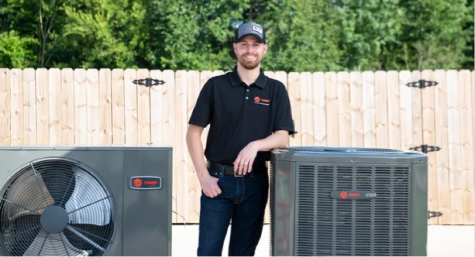 Trane technician standing with outdoor heat pump and air conditioner.
