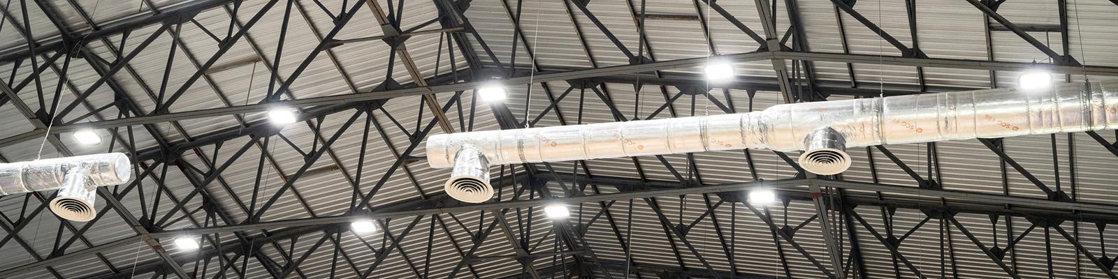 This is a photograph of an interior warehouse ceiling showing the support beams, lights and ventilation ducts.