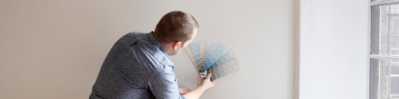 Man holds up paint samples against a beige wall.