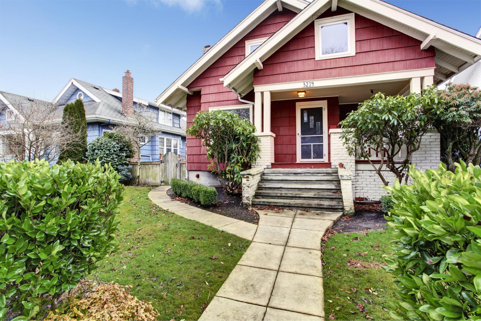 An older red Craftsman-style home. with a lush green yard.