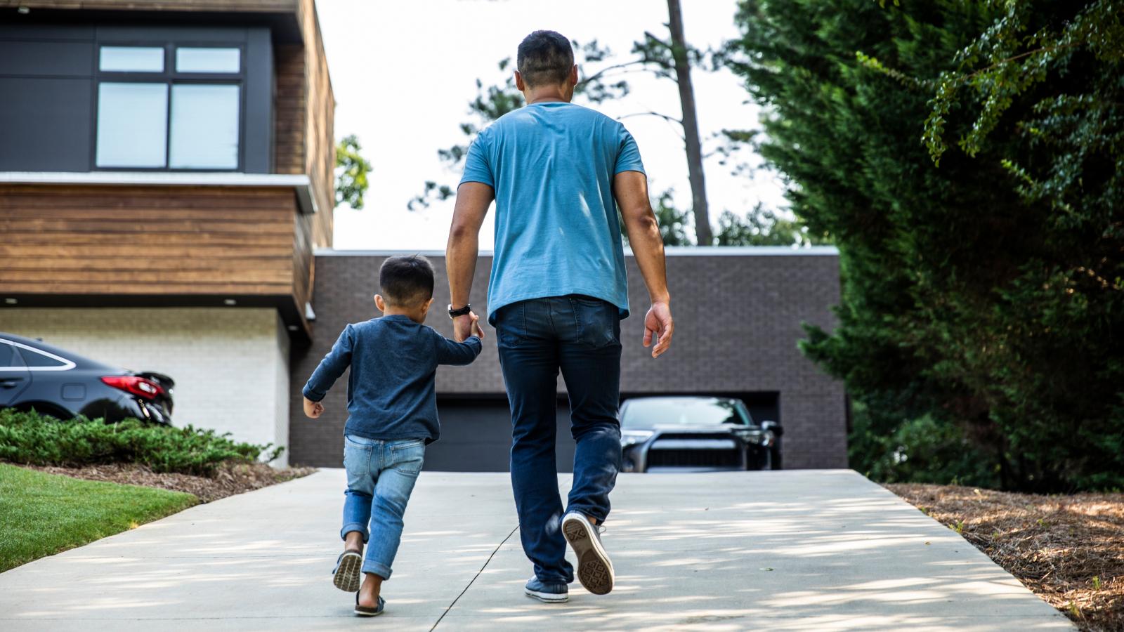 A father and son holding hands while walking up a driveway.