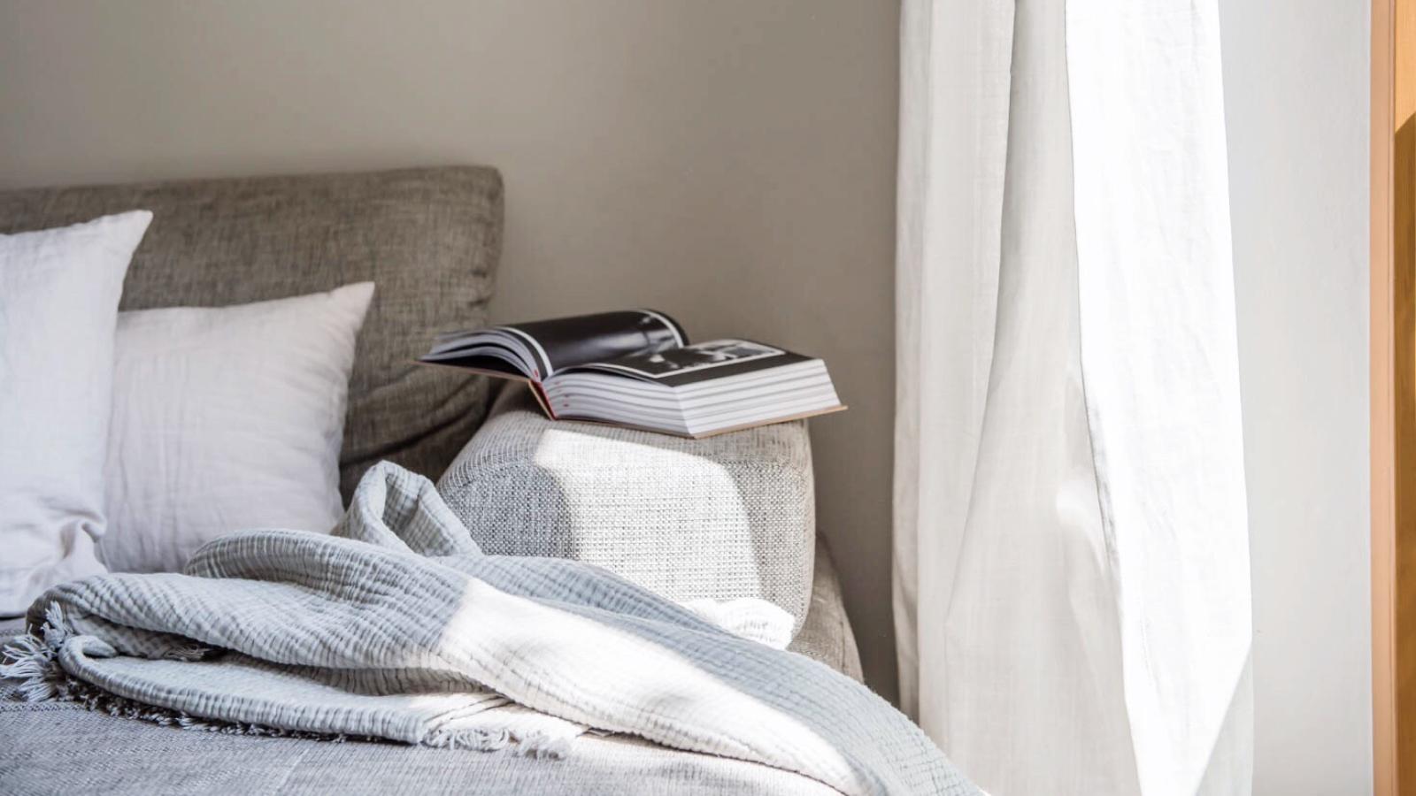 A black and white book is open on the arm of a gray couch.