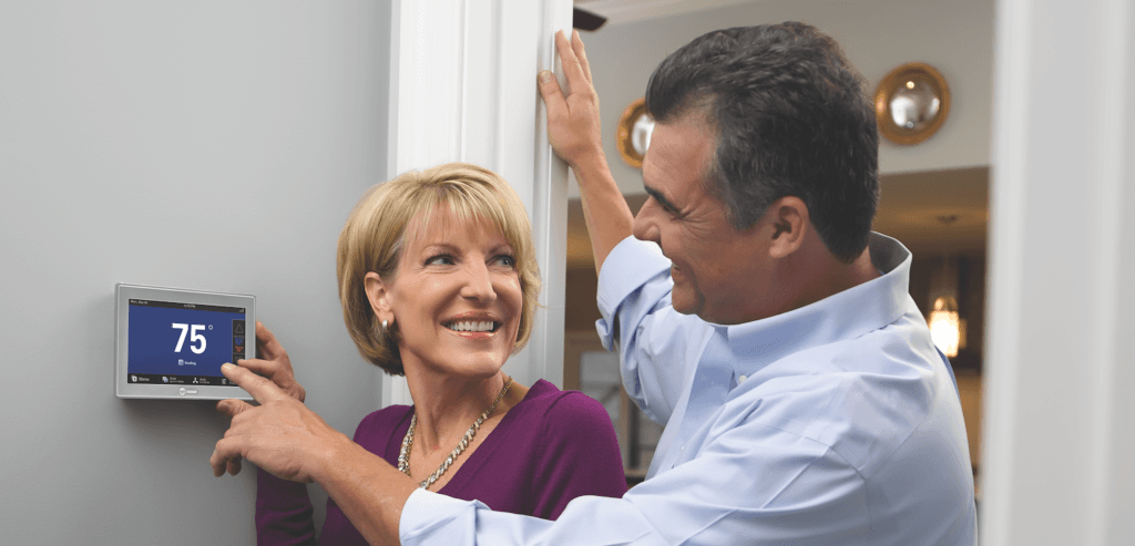 A woman and man smile in their home as their Trane smart thermostat reads a comfortable temperature of 75 degrees.