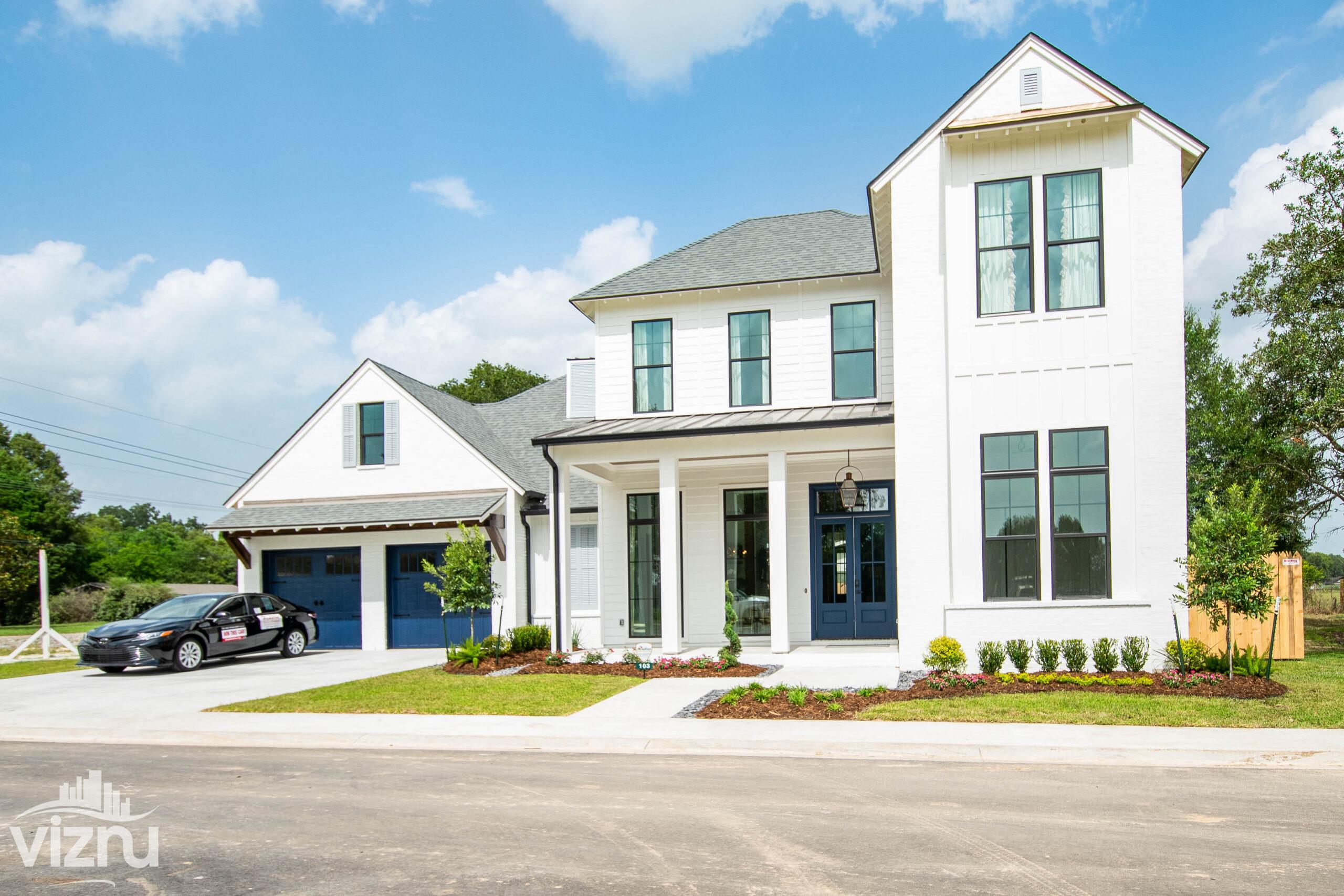 Large white home with blue doors and a car in the driveway is featured on a sunny day.