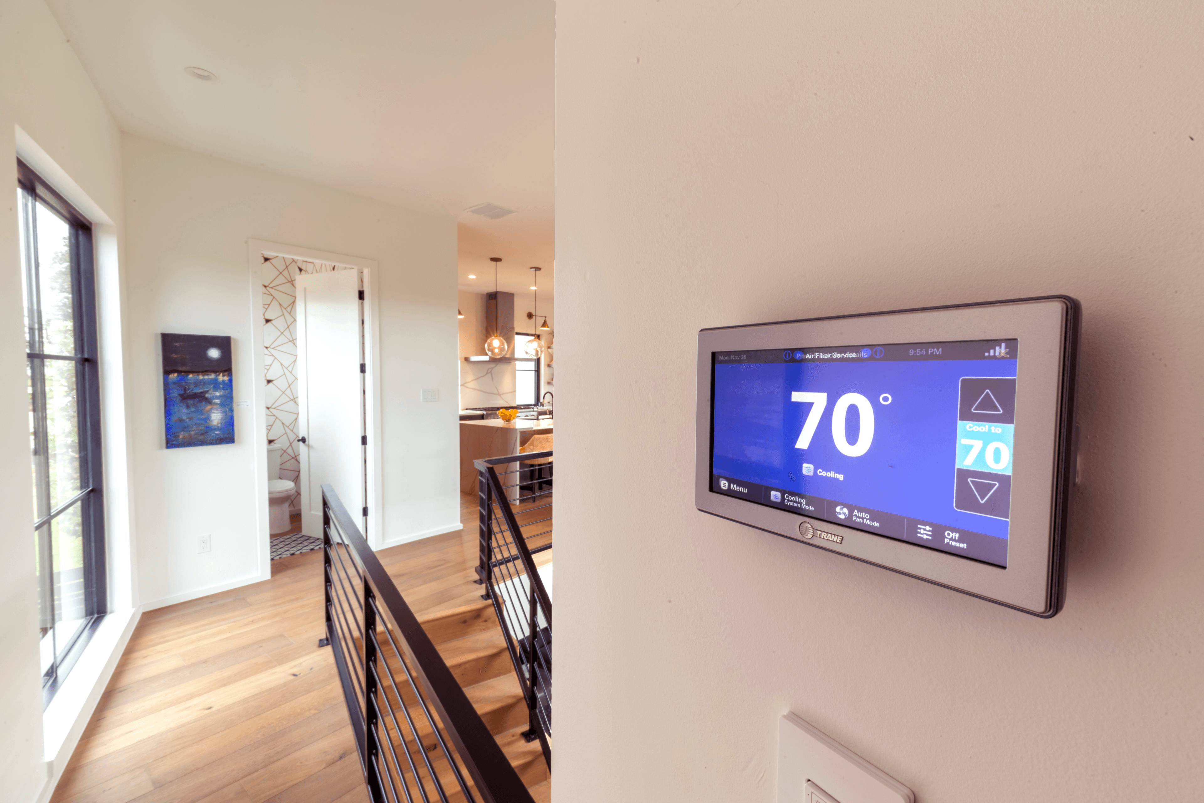 Trane smart thermostat reads 70 degrees inside a home with a bathroom and kitchen in the background.