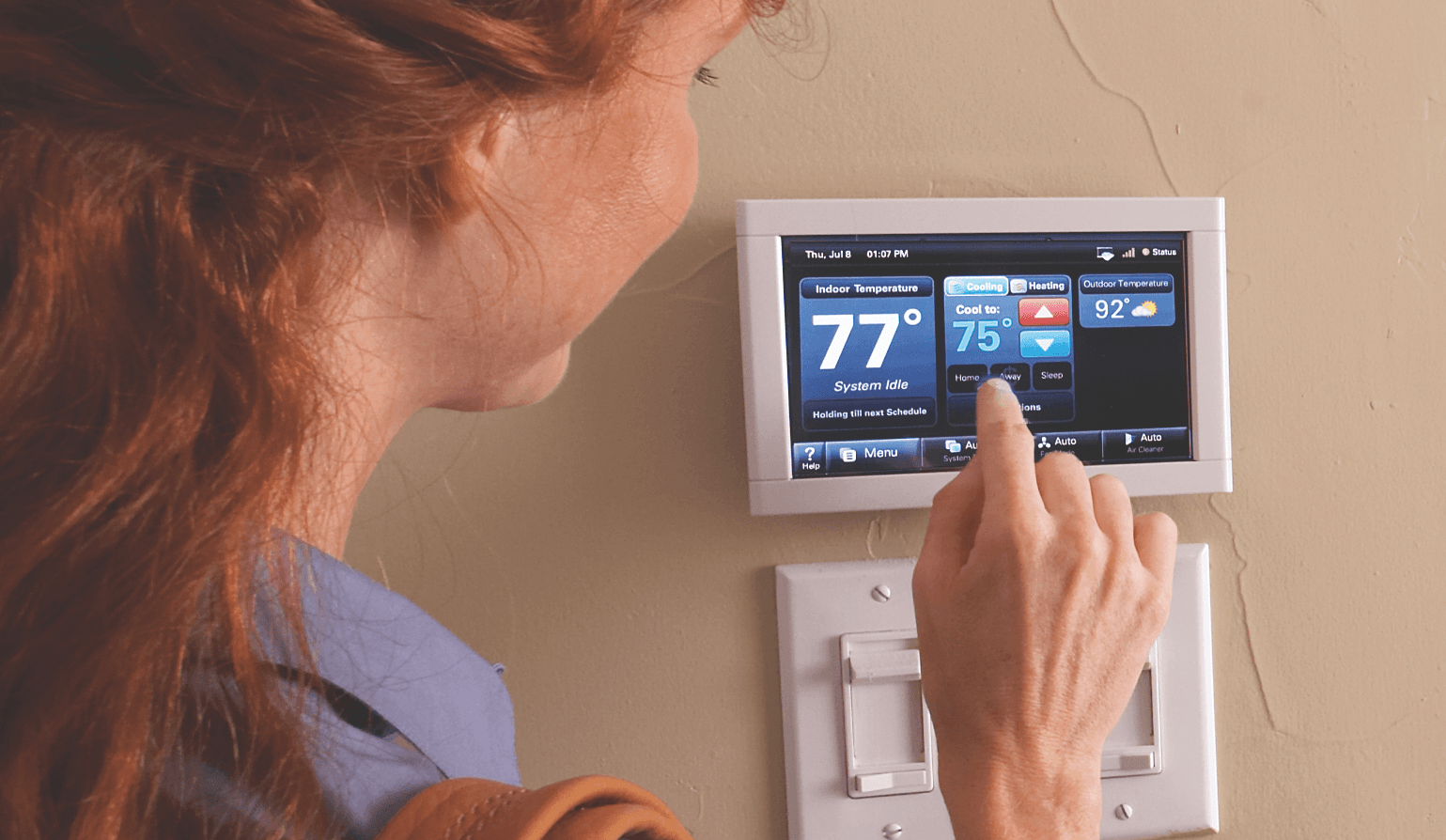 A woman changes her Trane smart thermostat from 77 degrees to 75 degrees.