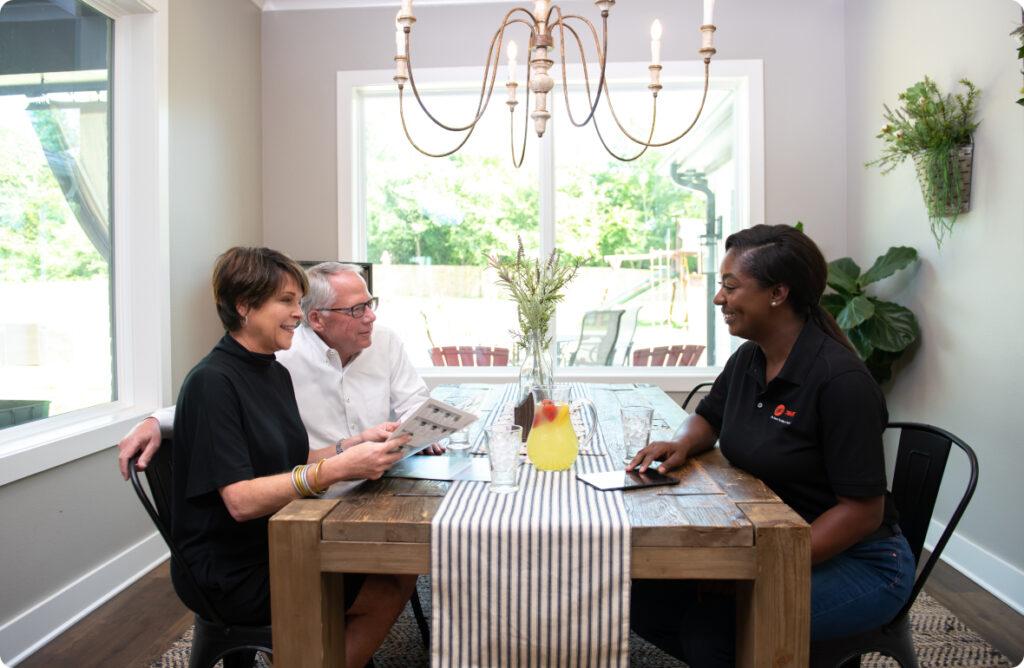 A man and woman sit at a dining table with a Trane HVAC technician.