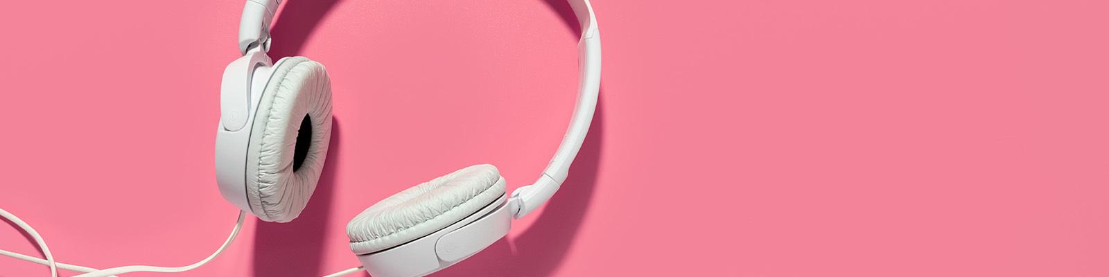 Large white headphones with cord lay on a bright pink background.