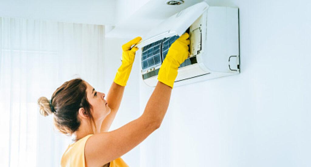 A woman performing maintenance on her ductless mini-split indoor unit.