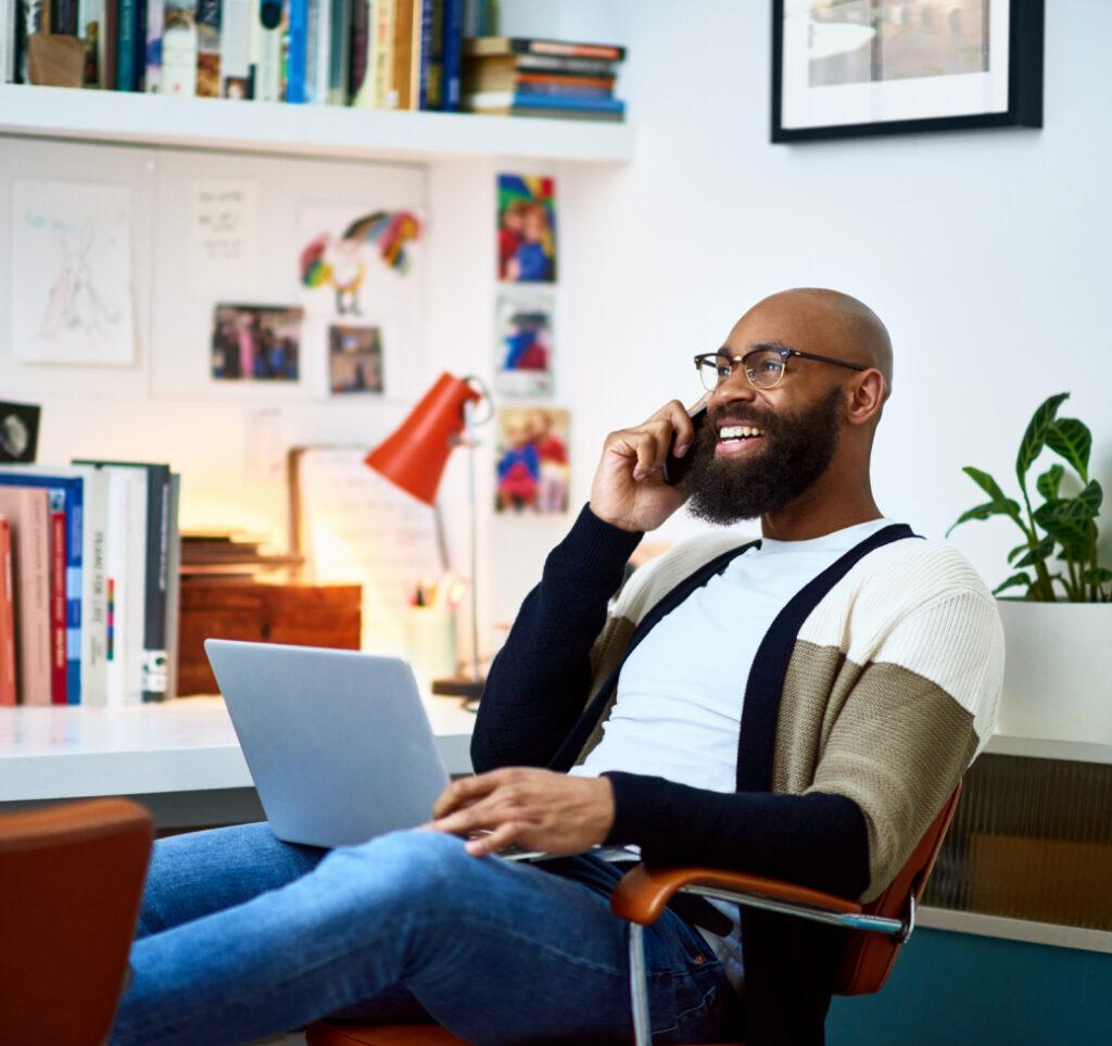 A man speaks on the telephone while holding a laptop.