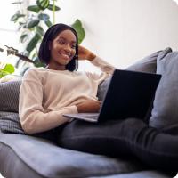 A woman laying on a sofa looking at a laptop.