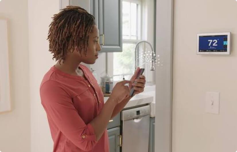 A woman using her cellular phone to change the temperature on her smart thermostat.