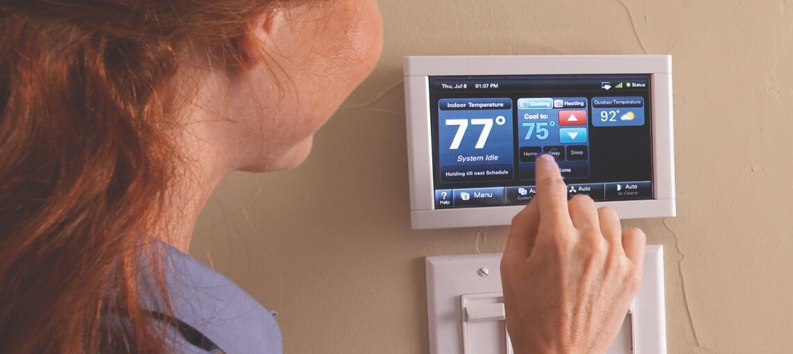 A woman changes the settings on her home thermostat.