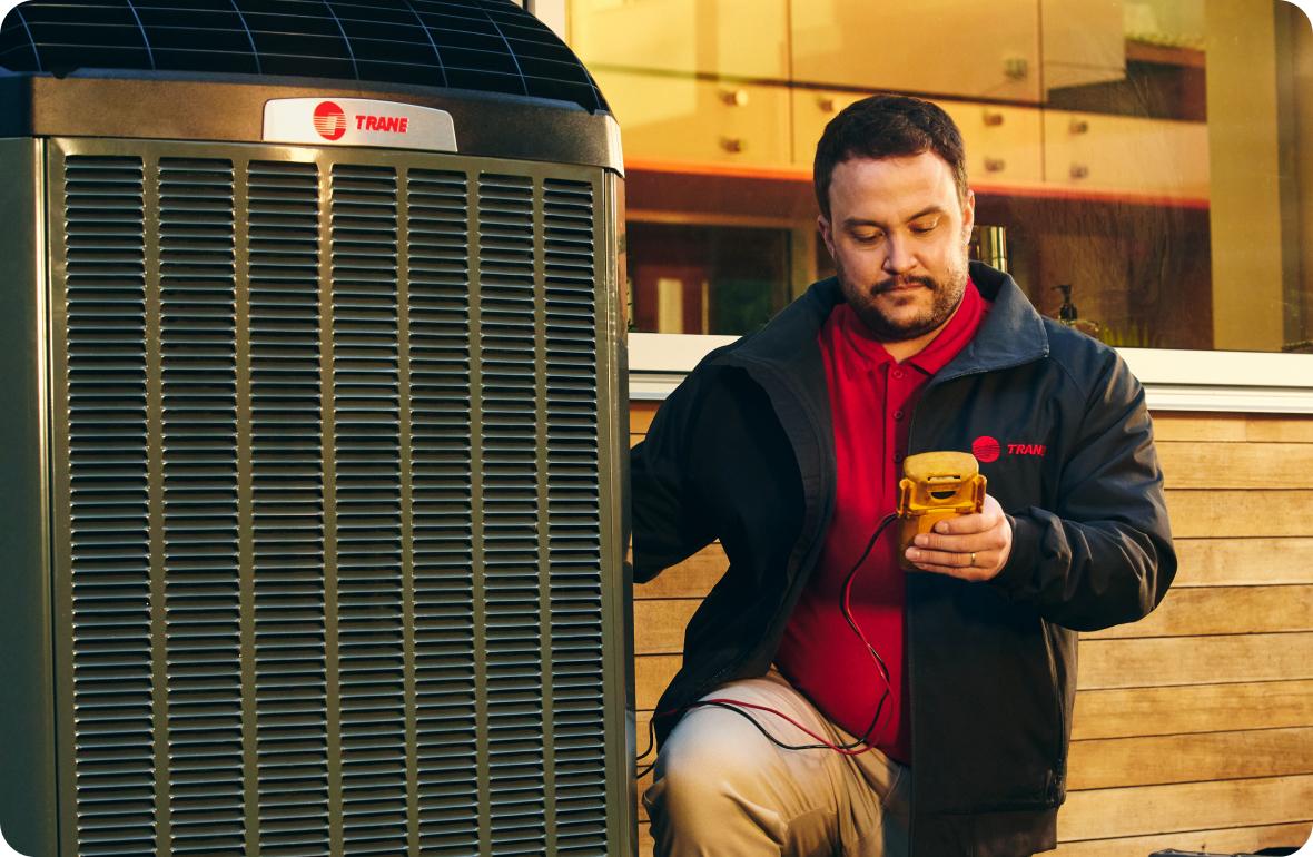 Trane HVAC professional inspecting a Trane branded outdoor central air conditioning unit.