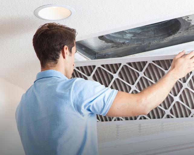 A young caucasian man in a blue shirt is changing a home air filter.