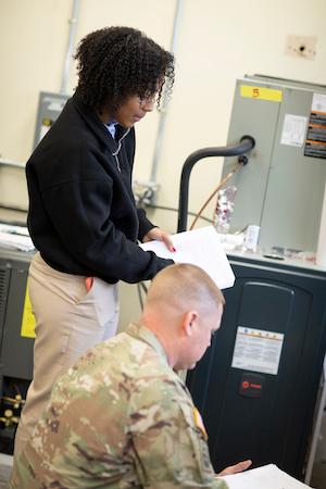 Two female Army personnel, an African American and caucasian are working on a home furnace unit