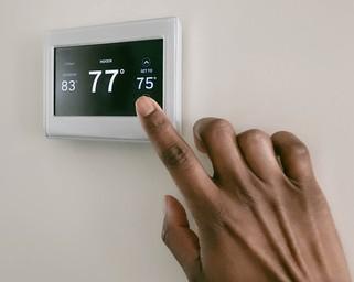 A young African American woman in a black and white striped shirt is setting her home thermostat on the wall.