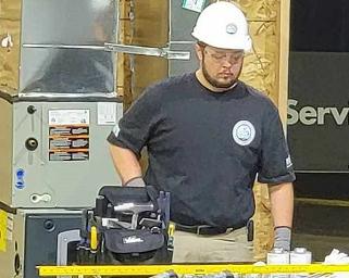 A Caucasian male in a black shirt is standing by a tool table.