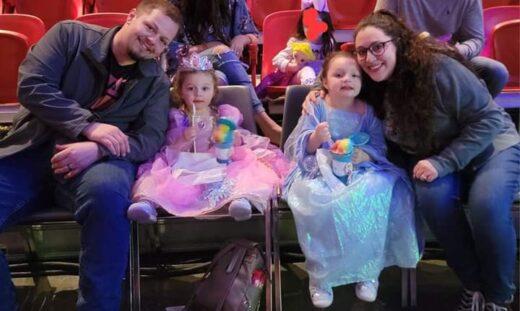 A young Caucasian man and woman are posing with their daughters in a movie theater.