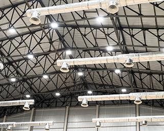 This is a photograph of an interior warehouse ceiling showing the support beams, lights and ventilation ducts.
