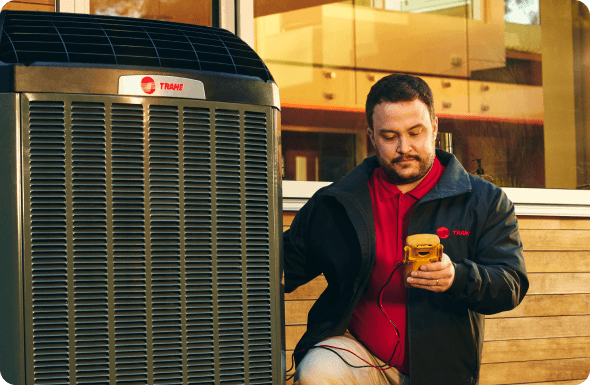 There is a Caucasian male Trane hvac tech inspecting a Trane home air conditioning unit.