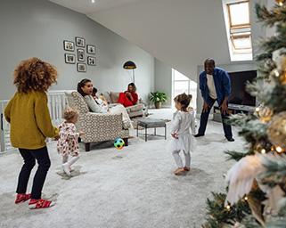 A young African American father is playing with his two young daughters by their Christmas tree in a white colored living room.