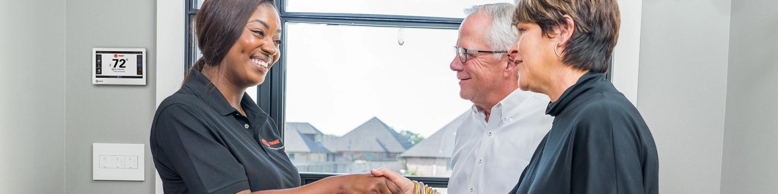 HVAC Technician and Homeowners in front of a Trane Smart Thermostat
