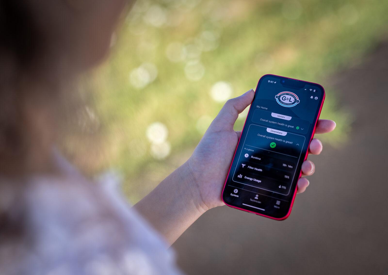 Homeowner Holding Phone with HVAC Performance Monitoring App Showing System Health Metrics