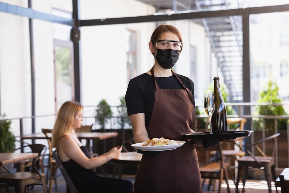 The waitress works in a restaurant in a medical mask, gloves during coronavirus pandemic