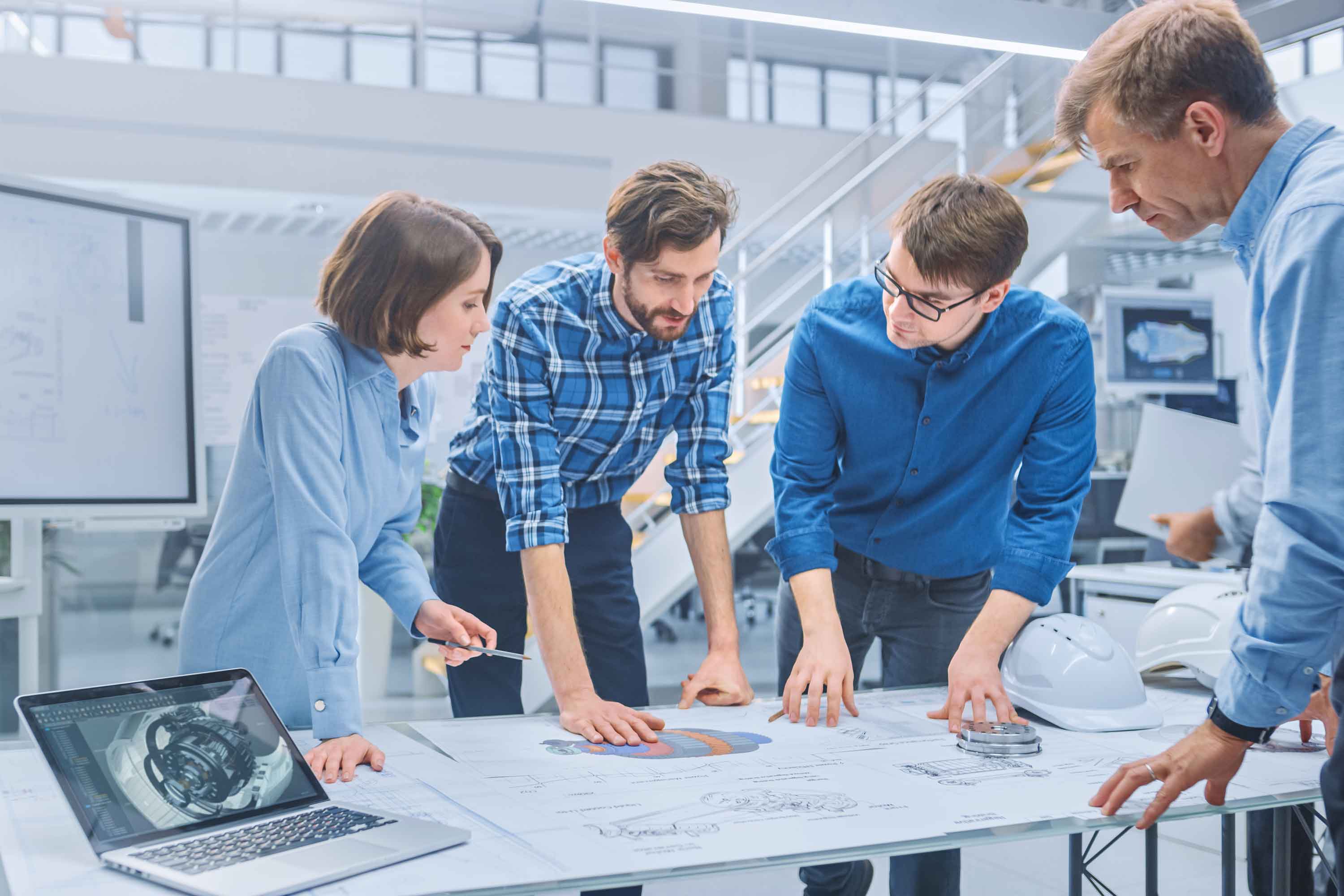 In the Industrial Engineering Facility: Diverse Group of Engineers and Technicians on a Meeting Gather Around Table with Engine Design Technical Drafts, Have Discussion, Analyse Technology