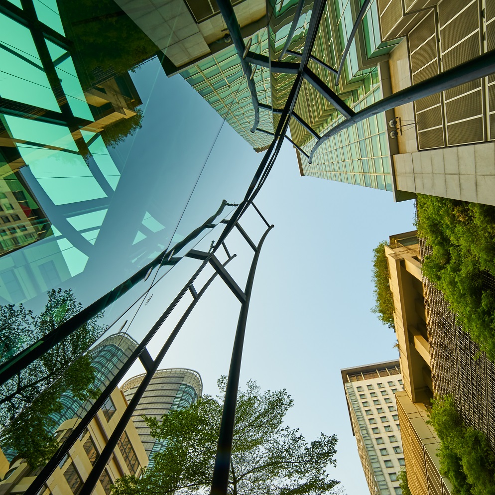 Low angle shot of modern glass buildings and green with clear sky background.