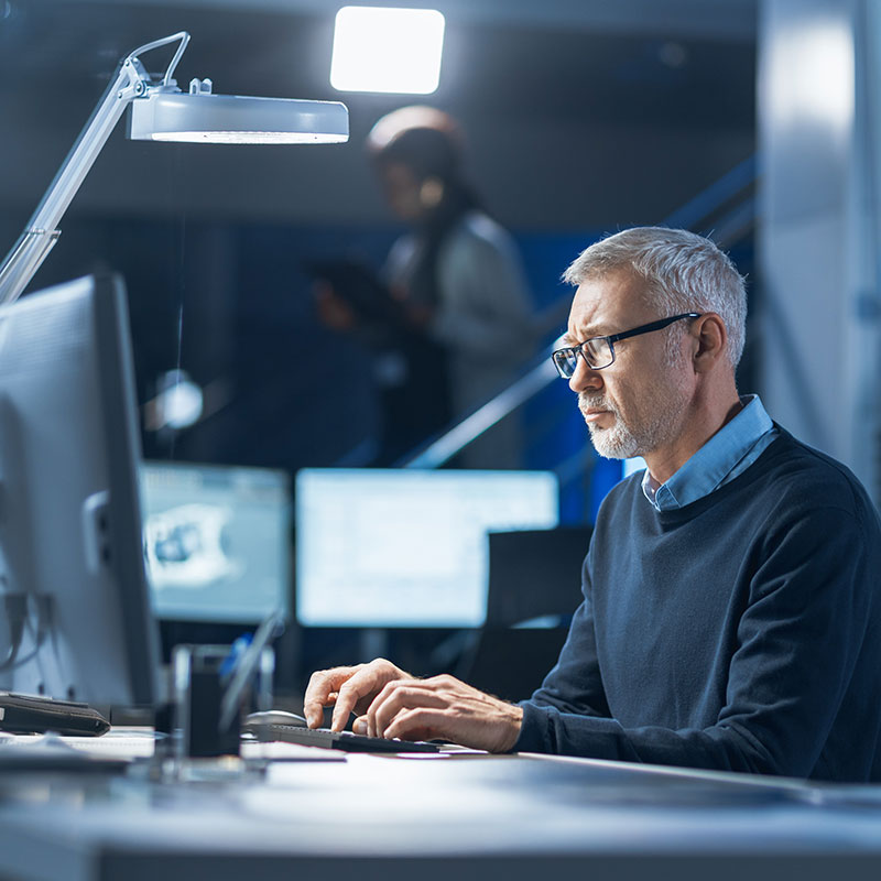 Shot of Industrial Engineer Working in Research Laboratory / Development Center, Using Computer. In the Background Technology Development Laboratory with Scientists, Engineers Working